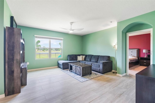 living room with ceiling fan, a textured ceiling, and light wood-type flooring