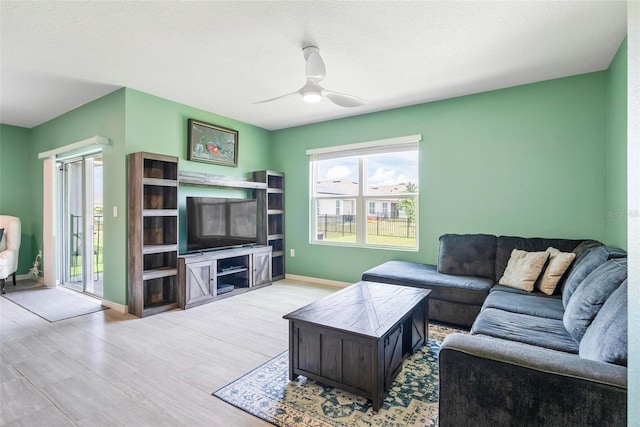 living room with a textured ceiling, ceiling fan, and light wood-type flooring