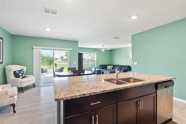 kitchen with dark brown cabinetry, sink, dishwasher, an island with sink, and light stone countertops