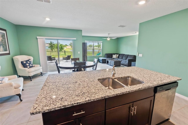 kitchen with sink, a kitchen island with sink, stainless steel dishwasher, dark brown cabinetry, and light stone counters