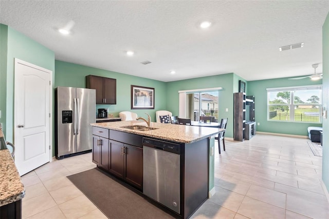 kitchen with a kitchen island with sink, light stone counters, dark brown cabinets, and stainless steel appliances