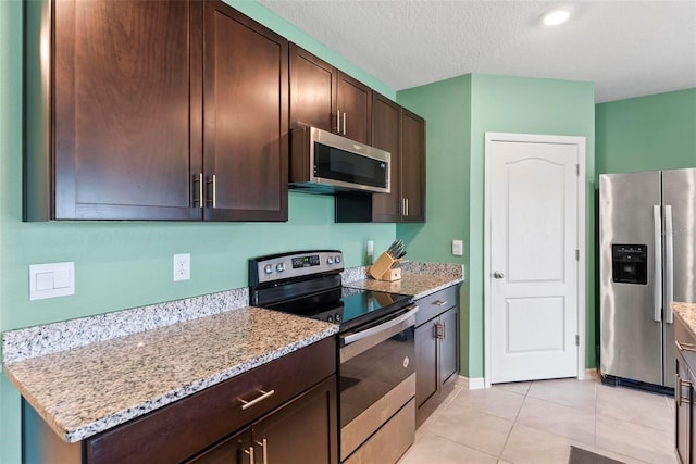 kitchen with light stone counters, light tile patterned floors, stainless steel appliances, and dark brown cabinetry