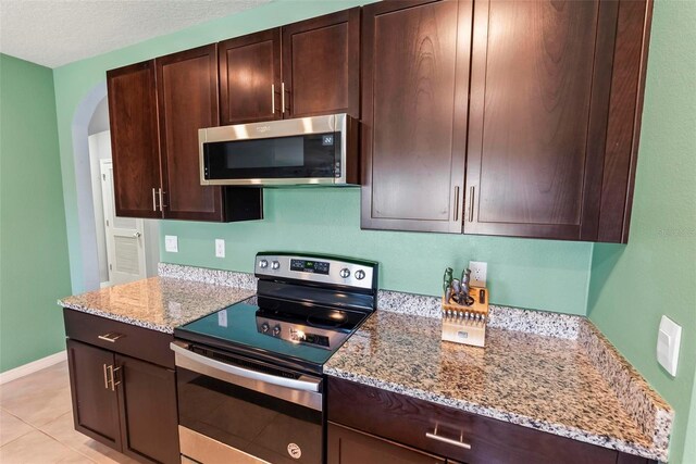 kitchen with light stone countertops, light tile patterned floors, dark brown cabinets, and stainless steel appliances