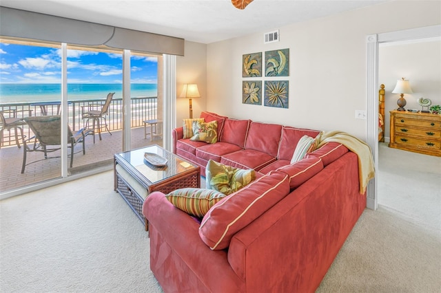 living room with carpet, a water view, and a beach view