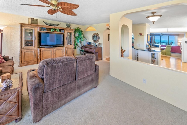 living room with a textured ceiling, light colored carpet, and ceiling fan