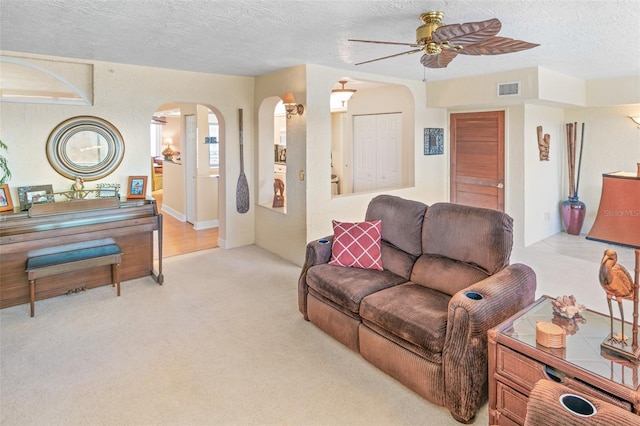 living room featuring light carpet, a textured ceiling, and ceiling fan