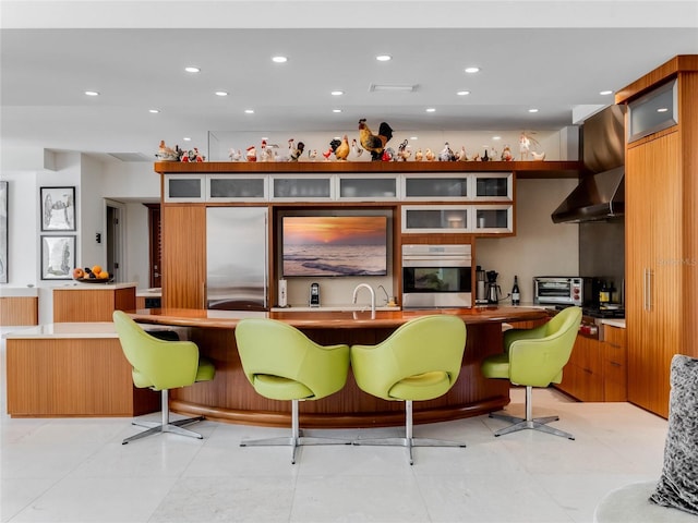 bar featuring light tile patterned flooring, wall chimney range hood, and appliances with stainless steel finishes