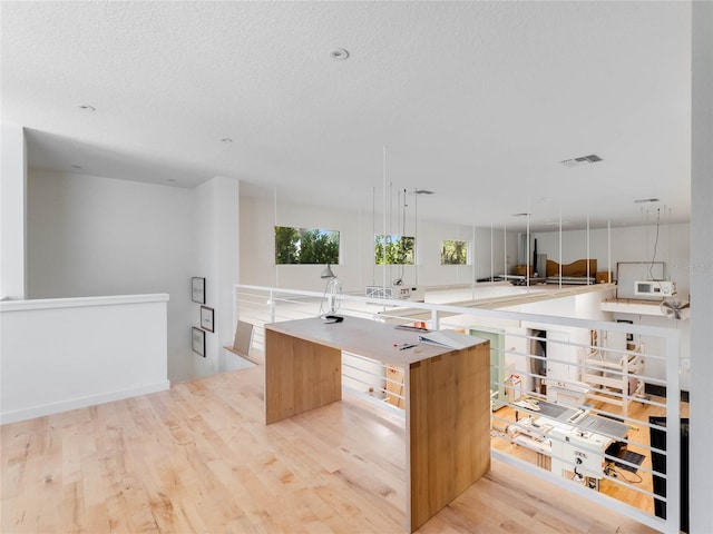 kitchen featuring a textured ceiling, a kitchen island with sink, and light hardwood / wood-style flooring