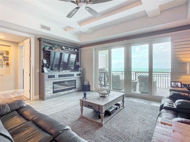 living room with visible vents, coffered ceiling, a high end fireplace, light wood finished floors, and ceiling fan