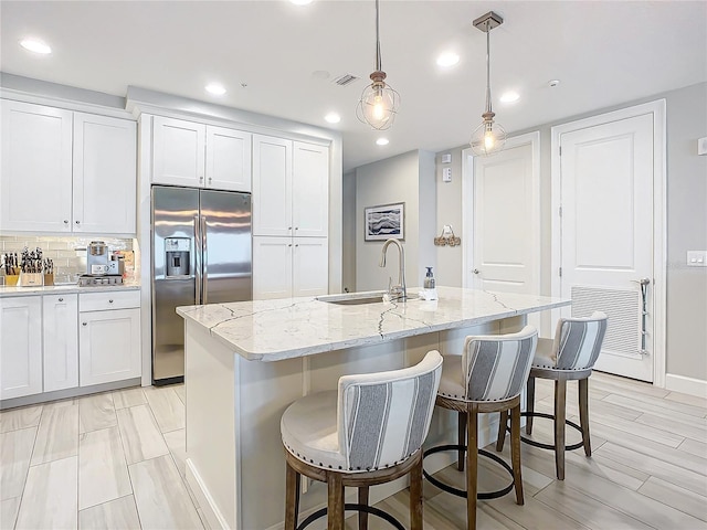 kitchen with decorative backsplash, light stone counters, stainless steel fridge with ice dispenser, and a sink