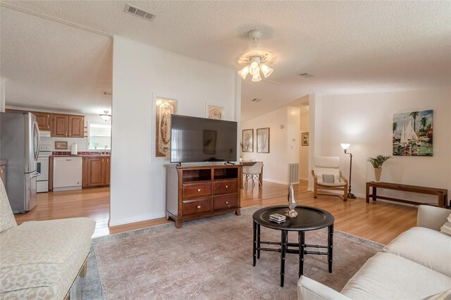 living room with a textured ceiling, light hardwood / wood-style floors, vaulted ceiling, and ceiling fan