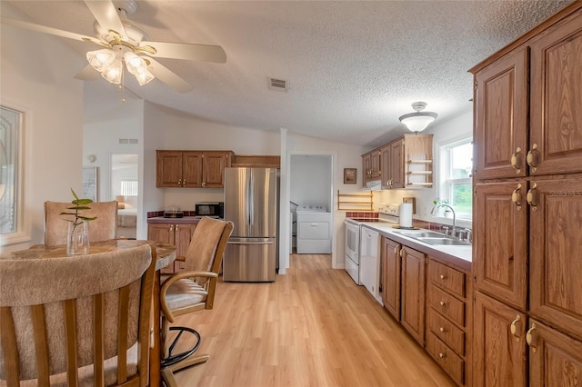 kitchen featuring sink, vaulted ceiling, light wood-type flooring, appliances with stainless steel finishes, and washer / dryer