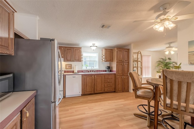 kitchen featuring ceiling fan, sink, light hardwood / wood-style flooring, a textured ceiling, and appliances with stainless steel finishes