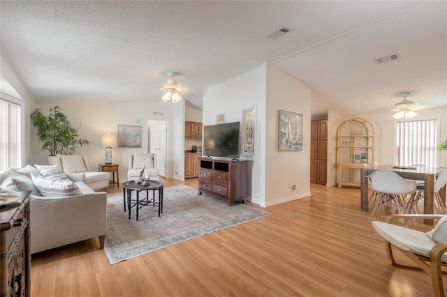 living room featuring ceiling fan, light wood-type flooring, lofted ceiling, and a textured ceiling