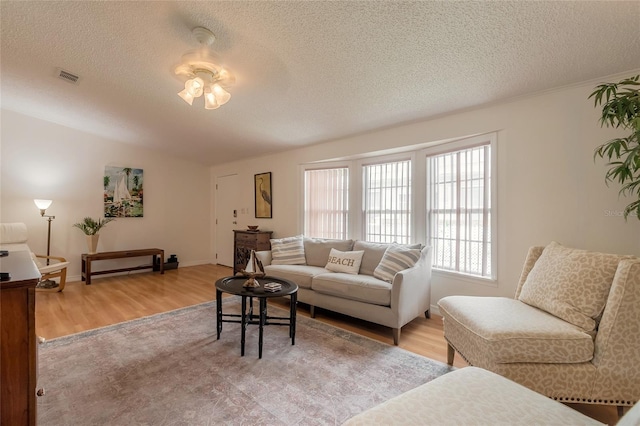 living room featuring ceiling fan, light wood-type flooring, and a textured ceiling