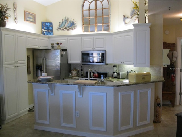 kitchen featuring decorative backsplash, white cabinets, appliances with stainless steel finishes, and dark stone countertops