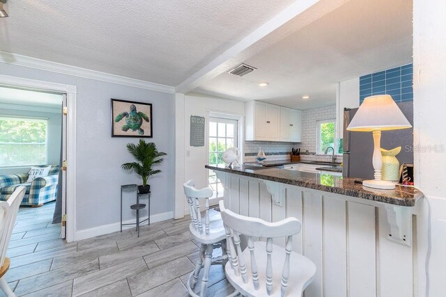 kitchen featuring dark stone counters, white cabinets, a kitchen breakfast bar, a textured ceiling, and kitchen peninsula