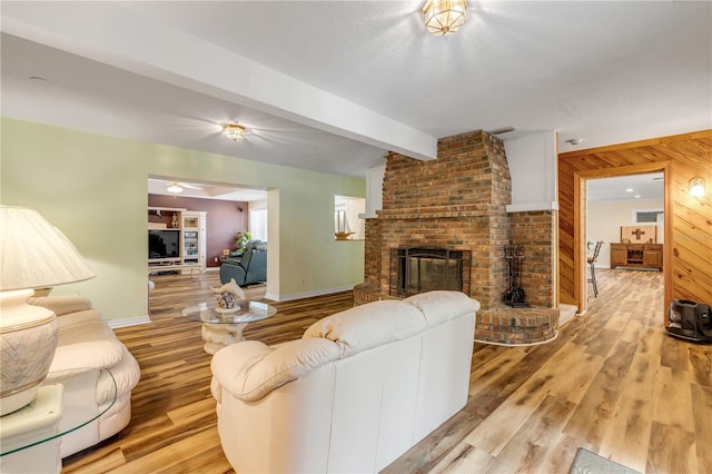 living room featuring beam ceiling, light wood-type flooring, a brick fireplace, and wood walls