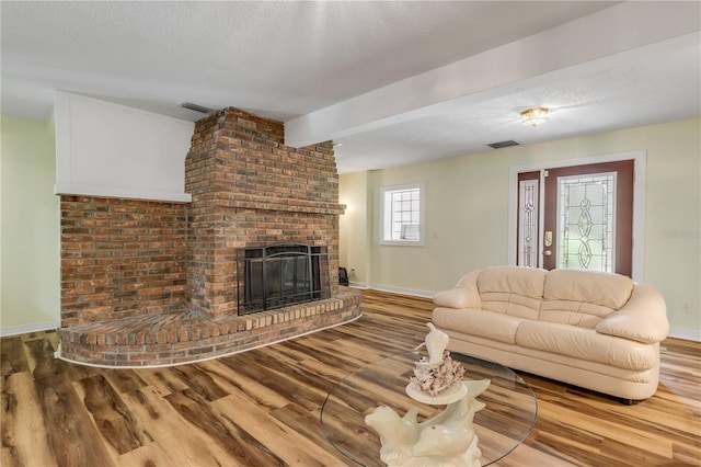 living room featuring a fireplace, wood-type flooring, a textured ceiling, and beamed ceiling