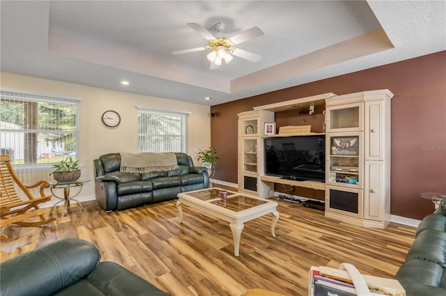 living room with a raised ceiling, ceiling fan, plenty of natural light, and light wood-type flooring