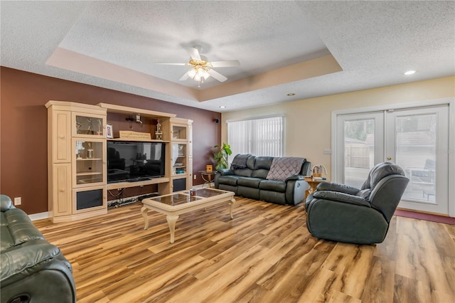 living room featuring a raised ceiling, light wood-type flooring, a textured ceiling, and french doors