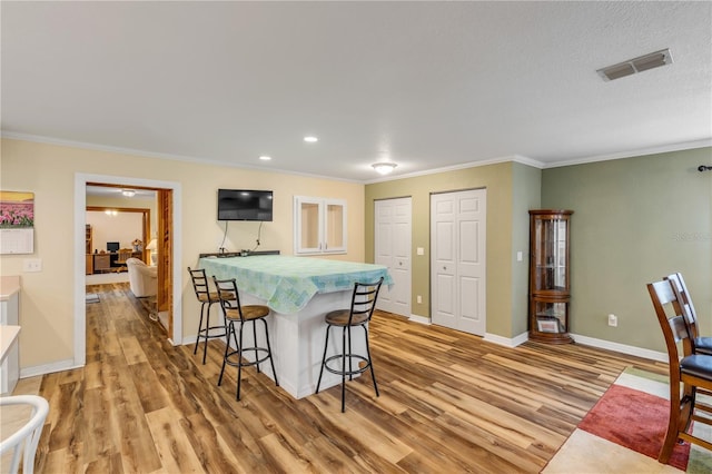 kitchen with a breakfast bar area, ornamental molding, a textured ceiling, and light wood-type flooring