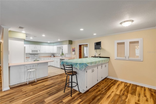 kitchen featuring kitchen peninsula, white appliances, white cabinetry, and a breakfast bar area