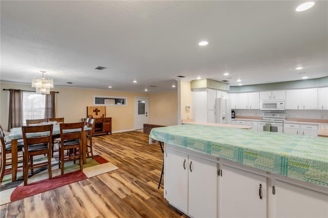 kitchen featuring white appliances, pendant lighting, an inviting chandelier, white cabinets, and light hardwood / wood-style floors