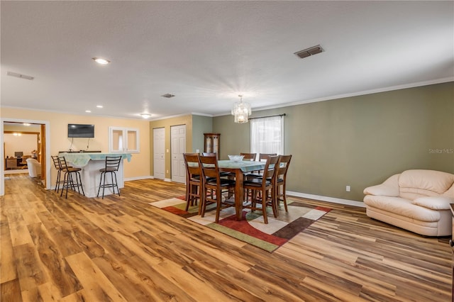 dining area with a notable chandelier, crown molding, and light hardwood / wood-style flooring