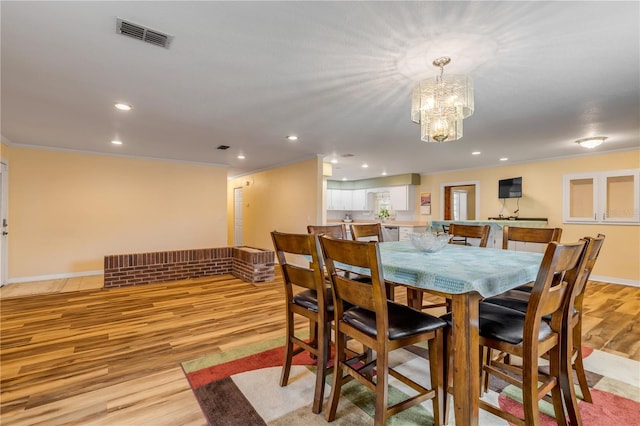 dining room with ornamental molding, light hardwood / wood-style floors, and a notable chandelier