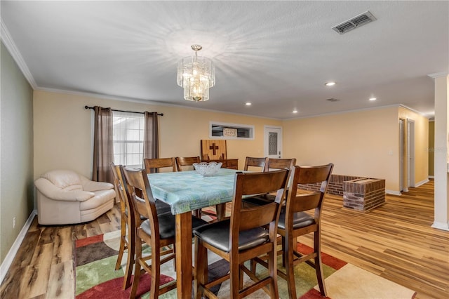 dining space with crown molding, light hardwood / wood-style flooring, and an inviting chandelier