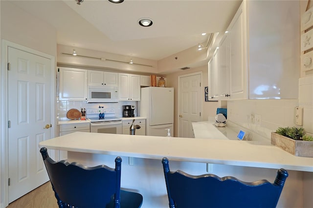 kitchen with kitchen peninsula, white appliances, white cabinets, and backsplash