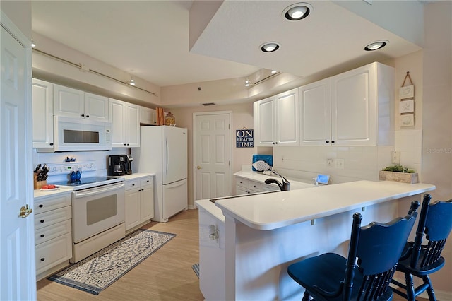 kitchen with kitchen peninsula, a kitchen bar, white appliances, and white cabinetry