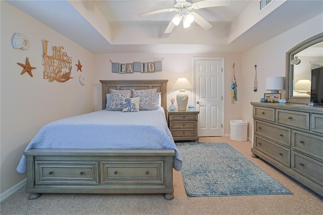 bedroom with ceiling fan, light colored carpet, and a tray ceiling