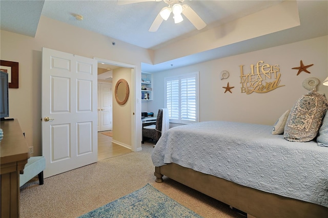 bedroom featuring ceiling fan, light carpet, and a tray ceiling