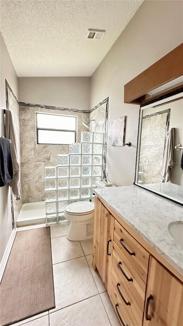 bathroom featuring tile patterned floors, a textured ceiling, toilet, tiled shower, and vanity