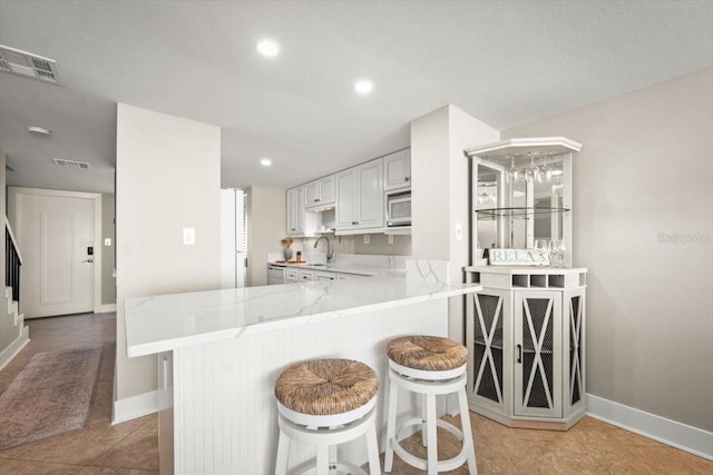 kitchen featuring a kitchen breakfast bar, kitchen peninsula, light tile patterned floors, light stone counters, and white cabinetry