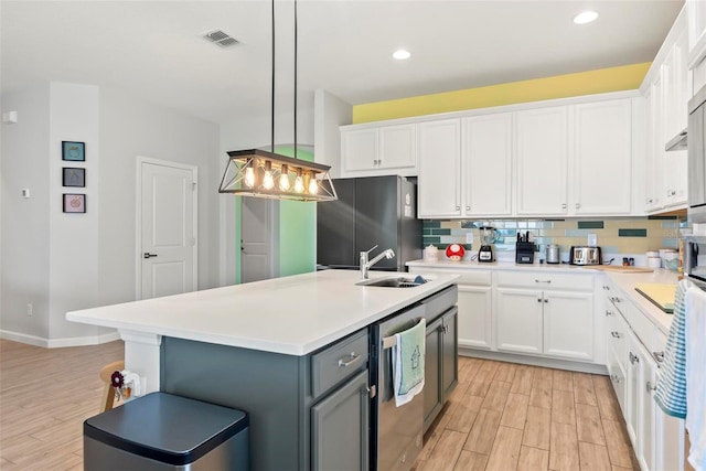 kitchen featuring sink, stainless steel fridge, pendant lighting, a center island with sink, and white cabinets