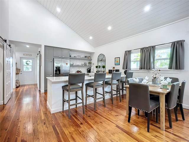 dining area featuring a barn door, light hardwood / wood-style flooring, high vaulted ceiling, and wood ceiling