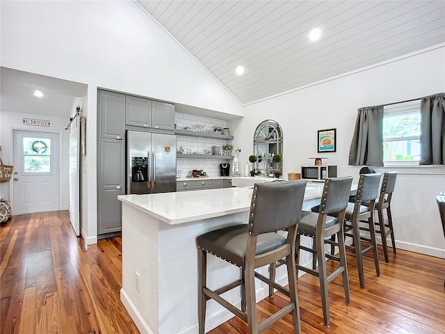 kitchen featuring gray cabinetry, a barn door, stainless steel refrigerator with ice dispenser, a kitchen bar, and wood ceiling