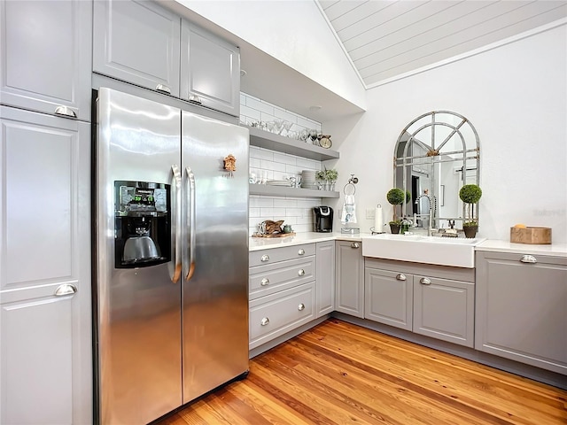 kitchen with gray cabinetry, sink, stainless steel refrigerator with ice dispenser, lofted ceiling, and light wood-type flooring