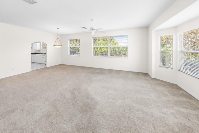 unfurnished living room with light carpet, visible vents, arched walkways, baseboards, and ceiling fan