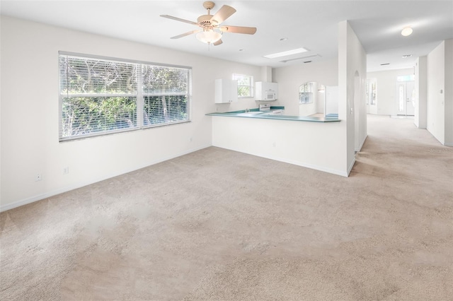 kitchen with ceiling fan, white microwave, light colored carpet, a peninsula, and white cabinets