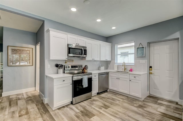 kitchen with appliances with stainless steel finishes, light hardwood / wood-style floors, backsplash, and white cabinetry