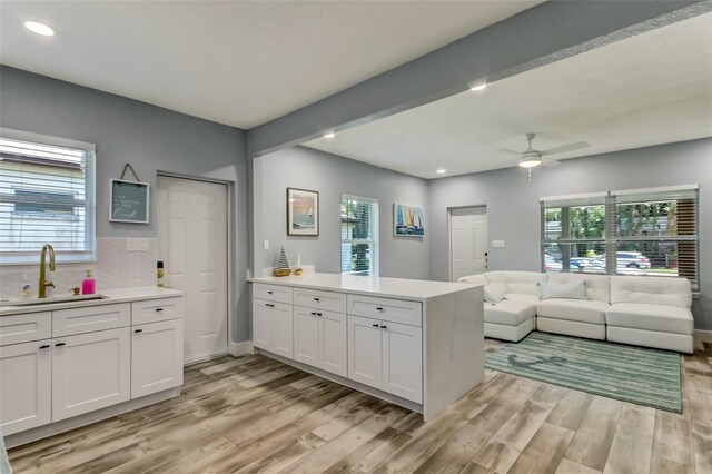 kitchen with ceiling fan, beamed ceiling, light wood-type flooring, sink, and white cabinets