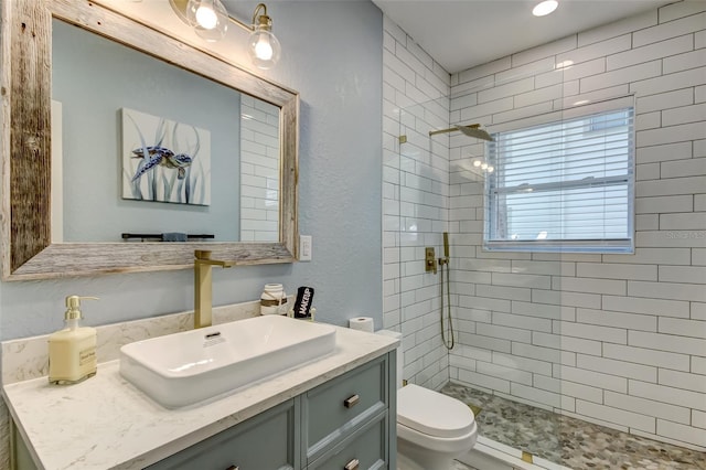 bathroom with a tile shower, vanity, and toilet