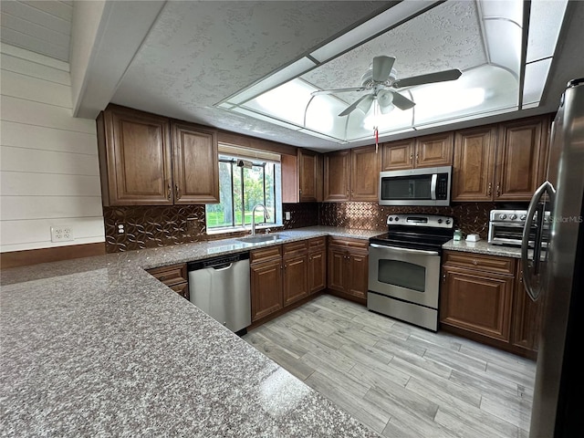 kitchen with decorative backsplash, appliances with stainless steel finishes, light wood-type flooring, ceiling fan, and sink