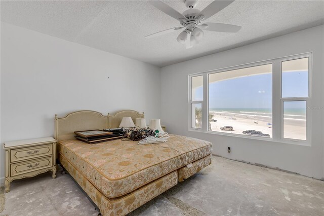 bedroom featuring a water view, a textured ceiling, a beach view, and ceiling fan