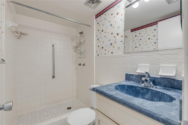 bathroom with tiled shower, vanity, toilet, and tile walls