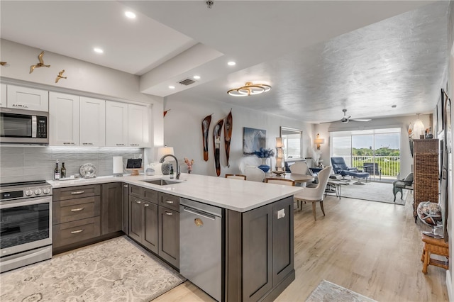 kitchen featuring kitchen peninsula, stainless steel appliances, ceiling fan, sink, and white cabinetry